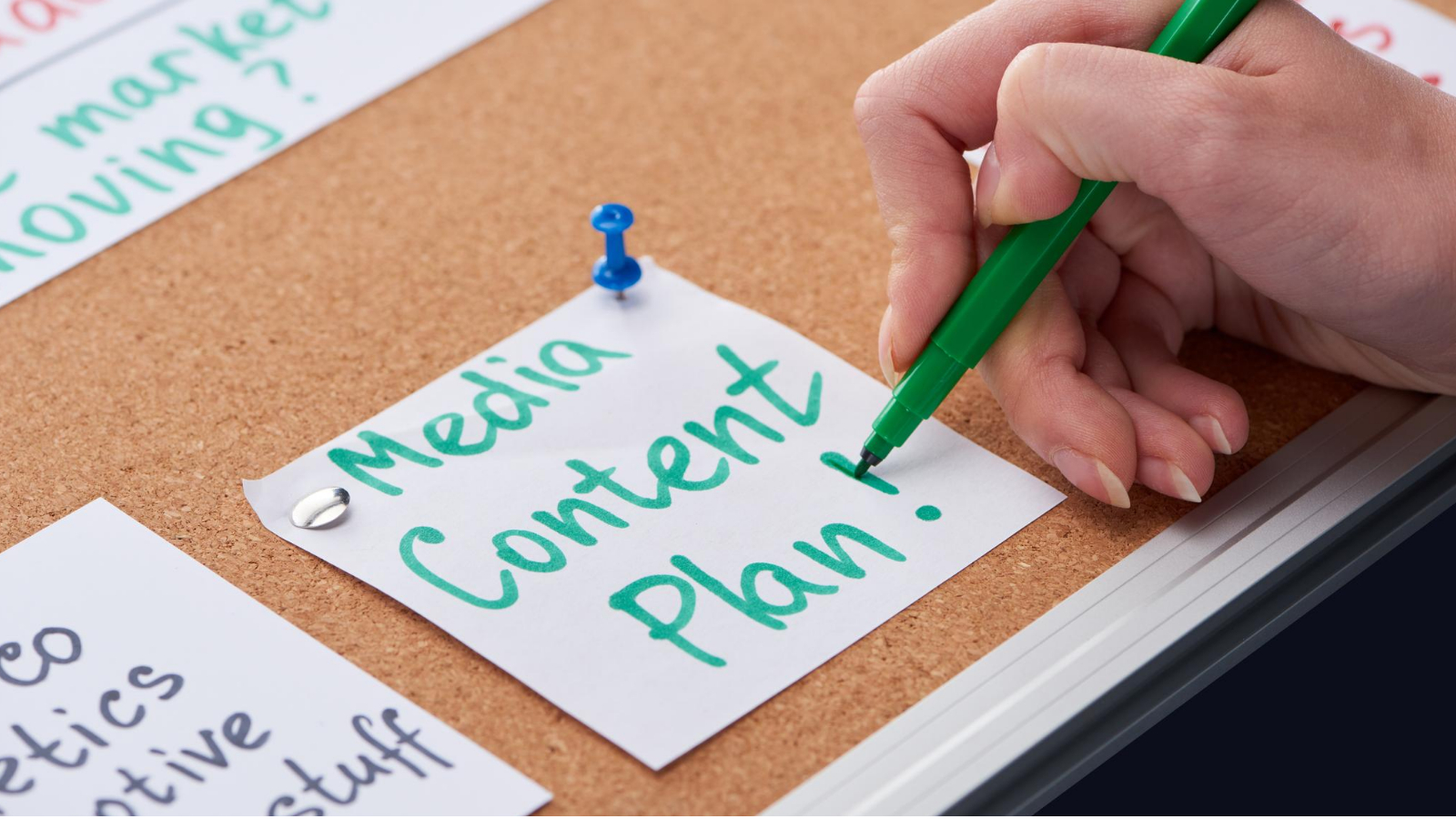 person sits at a desk, sketching out their media content plan on a sticky note